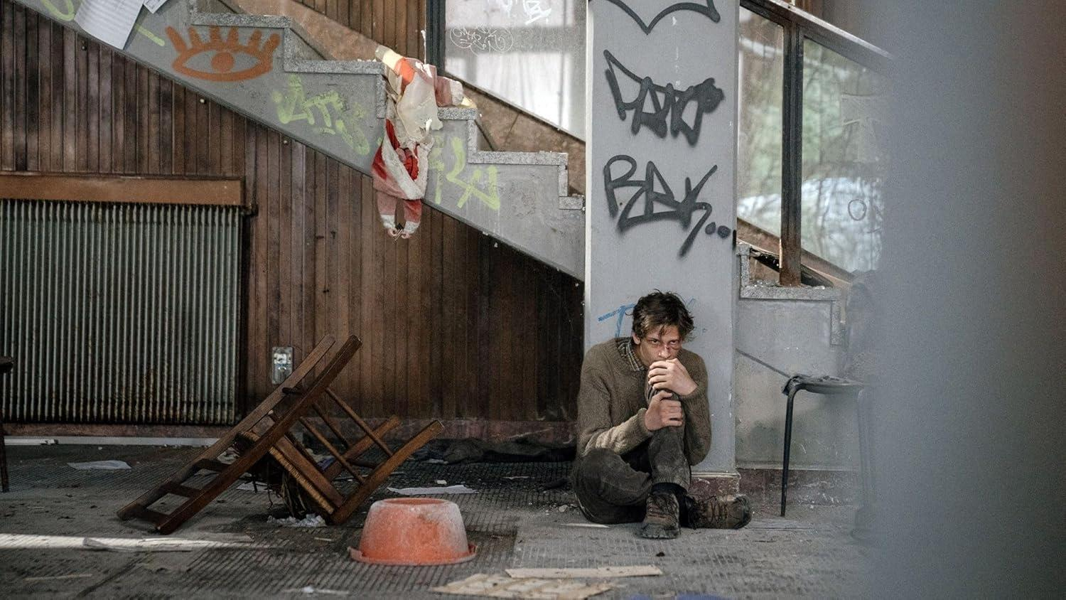Ein Mann sitzt auf dem Boden in einem verlassenen Gebäude mit Graffiti.