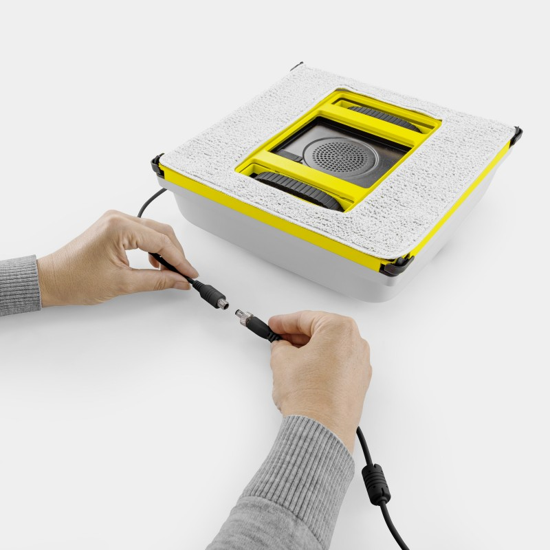 Dwie ręce podłączają dwa czarne kable do białego i żółtego urządzenia.