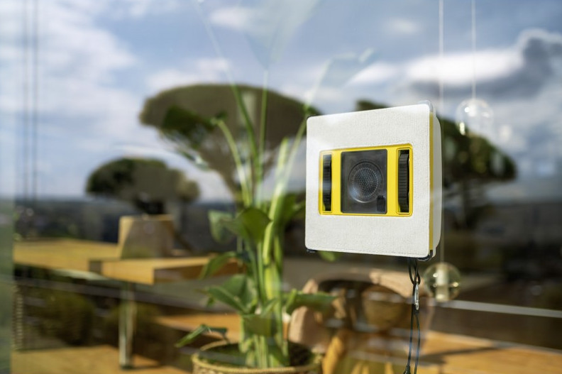 Biały robot do czyszczenia okien z żółtymi akcentami przywiera do okna.