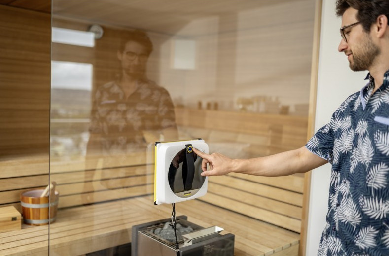 Mężczyzna w koszuli we wzory obsługuje robota do czyszczenia okien na szklanych drzwiach.