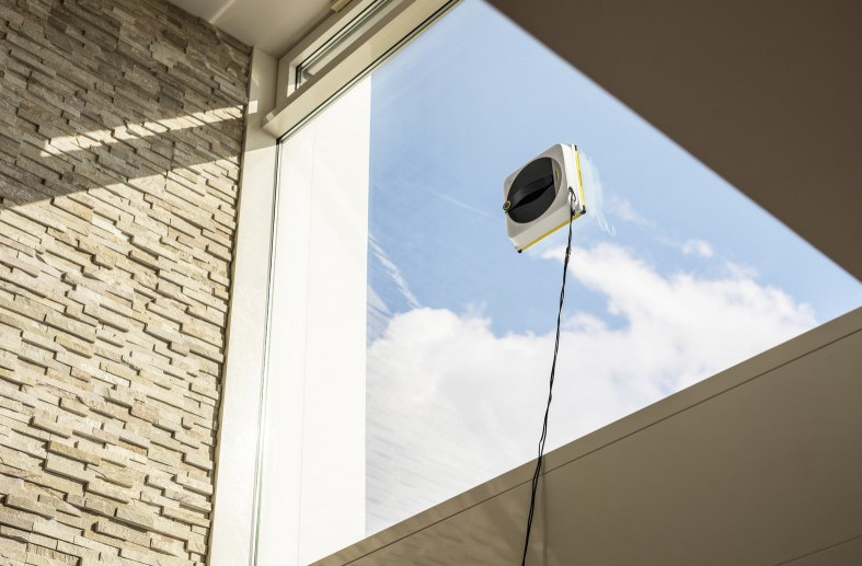 Robot do mycia okien działa na dużym oknie z niebem w tle.