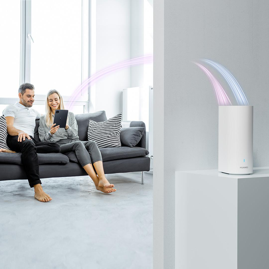 Ein Paar sitzt auf einem Sofa und schaut auf ein Tablet. Ein weißer Router sendet Lichtströme aus.