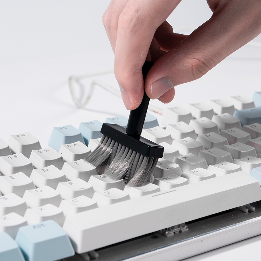 Eine Hand reinigt eine weiße Tastatur mit einer schwarzen Bürste.