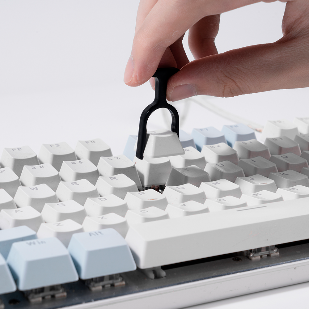 Eine Hand benutzt einen schwarzen Werkzeuggriff, um eine weiße Tastenkappe von einer Tastatur zu entfernen.