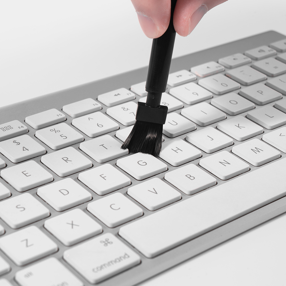 Eine Hand hält eine Bürste, um eine weiße Computertastatur zu reinigen.