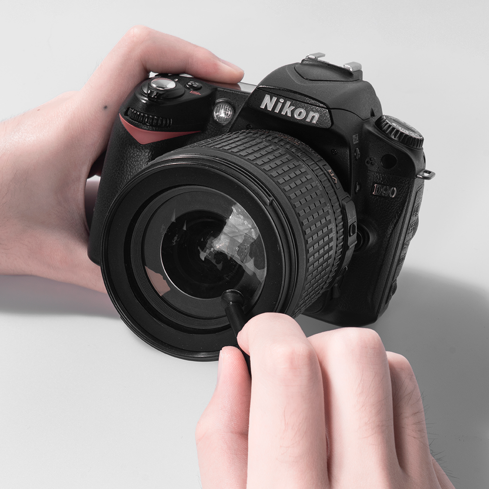 Hände reinigen ein Nikon D40 mit einem Objektiv-Reinigungswerkzeug.