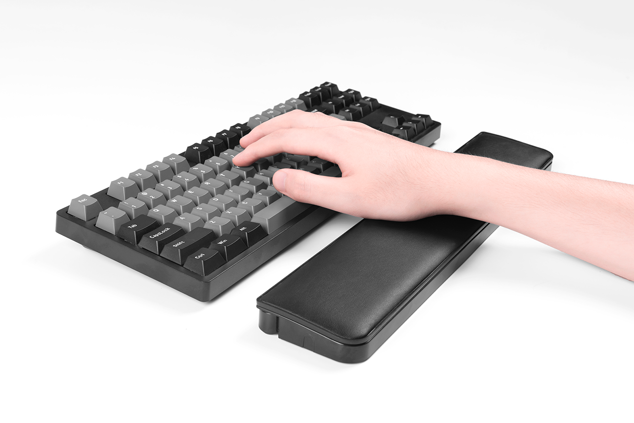 Hand auf Tastatur, Arm auf Handgelenkauflage, weier Hintergrund.