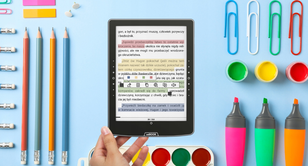 Czytnik e-booków na niebieskim tle otoczony artykułami piśmienniczymi.