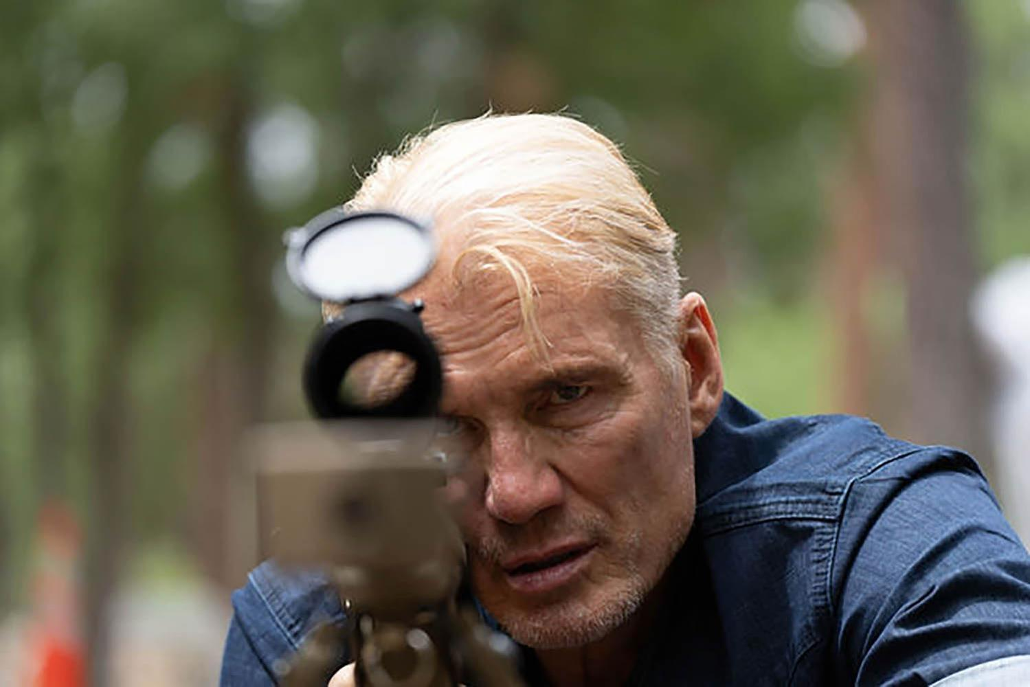 Ein Mann mit blonden Haaren zielt durch ein Fernglas auf etwas.