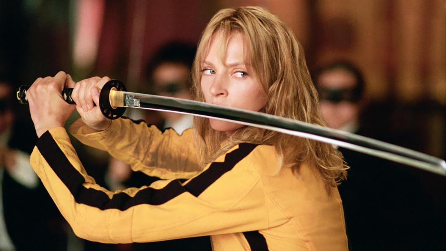 Eine Frau im gelben Anzug mit schwarzen Streifen hält ein Samuraischwert.