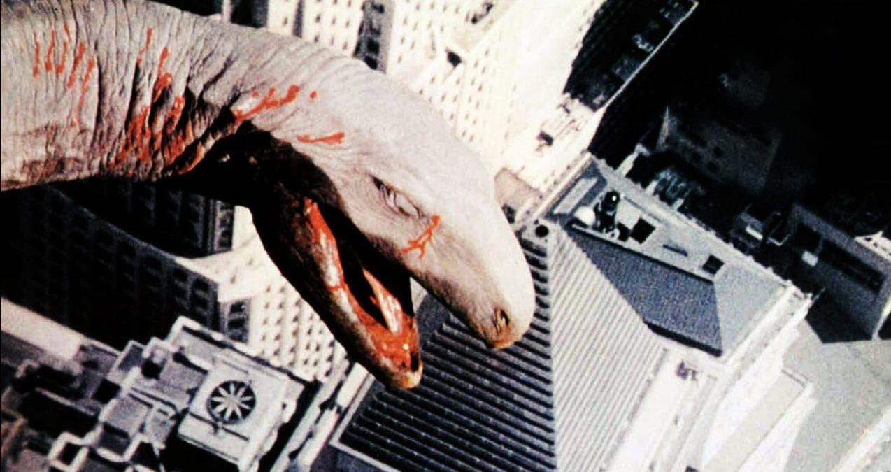 Ein riesiger Dino mit roten Flecken ragt über einer Stadt auf.