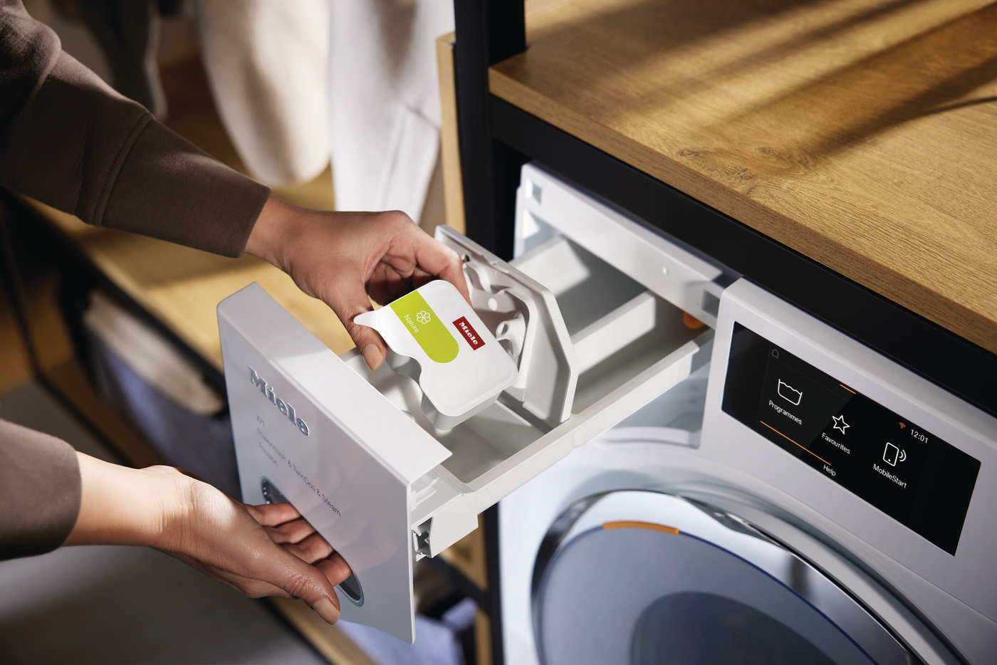 Eine Hand legt eine Miele Waschmittelkapsel in die Waschmaschine ein.