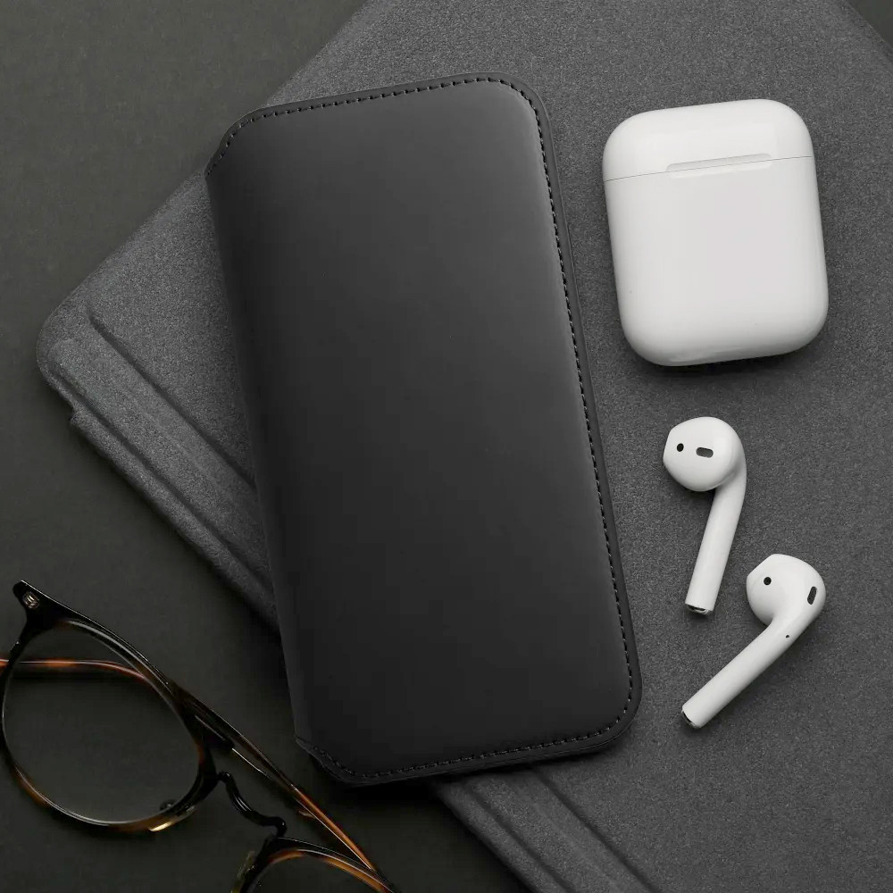 Fekete tok, AirPods, töltőtok és szemüveg sötét felületen.