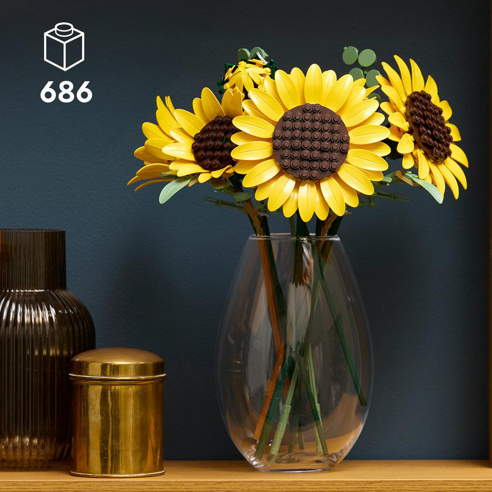 LEGO Sonnenblumen in einer Glasvase auf einem Regal, neben einer goldenen Dose.