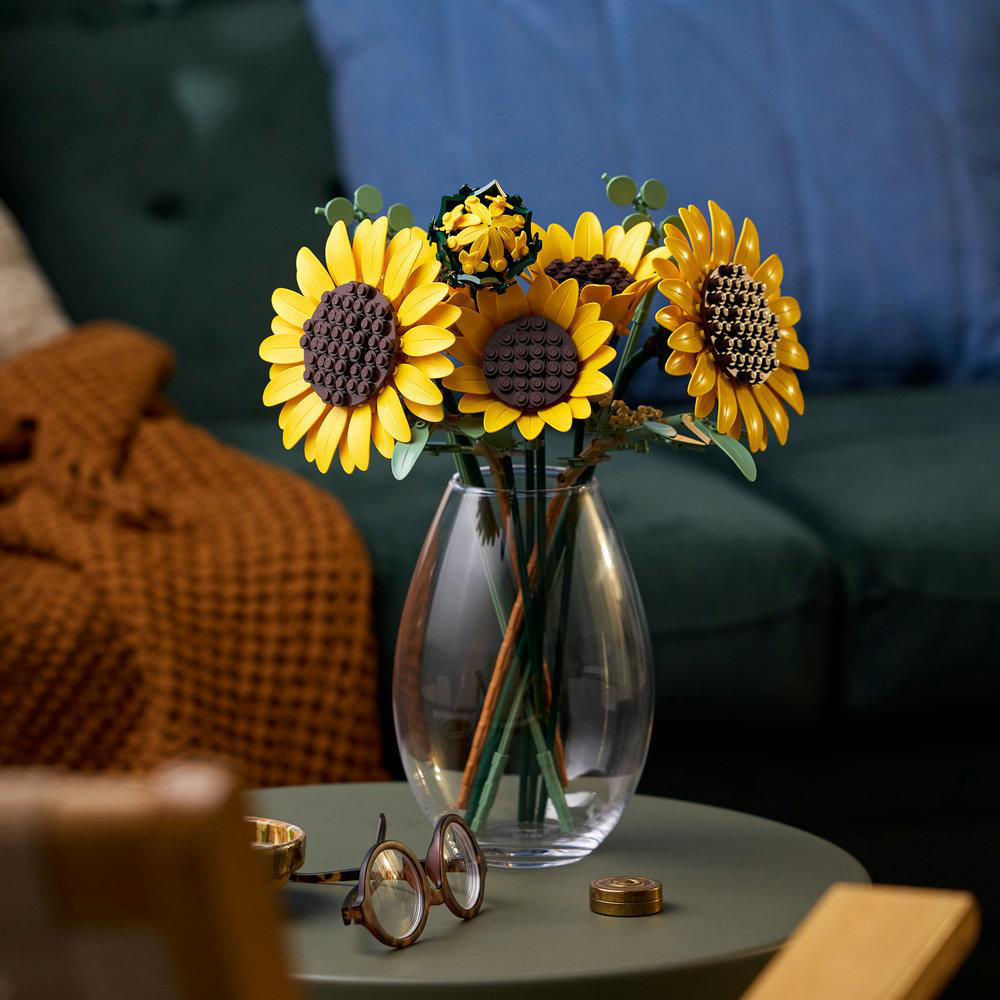 Ein Glasvase mit gelben Sonnenblumen steht auf einem Tisch mit Brille.
