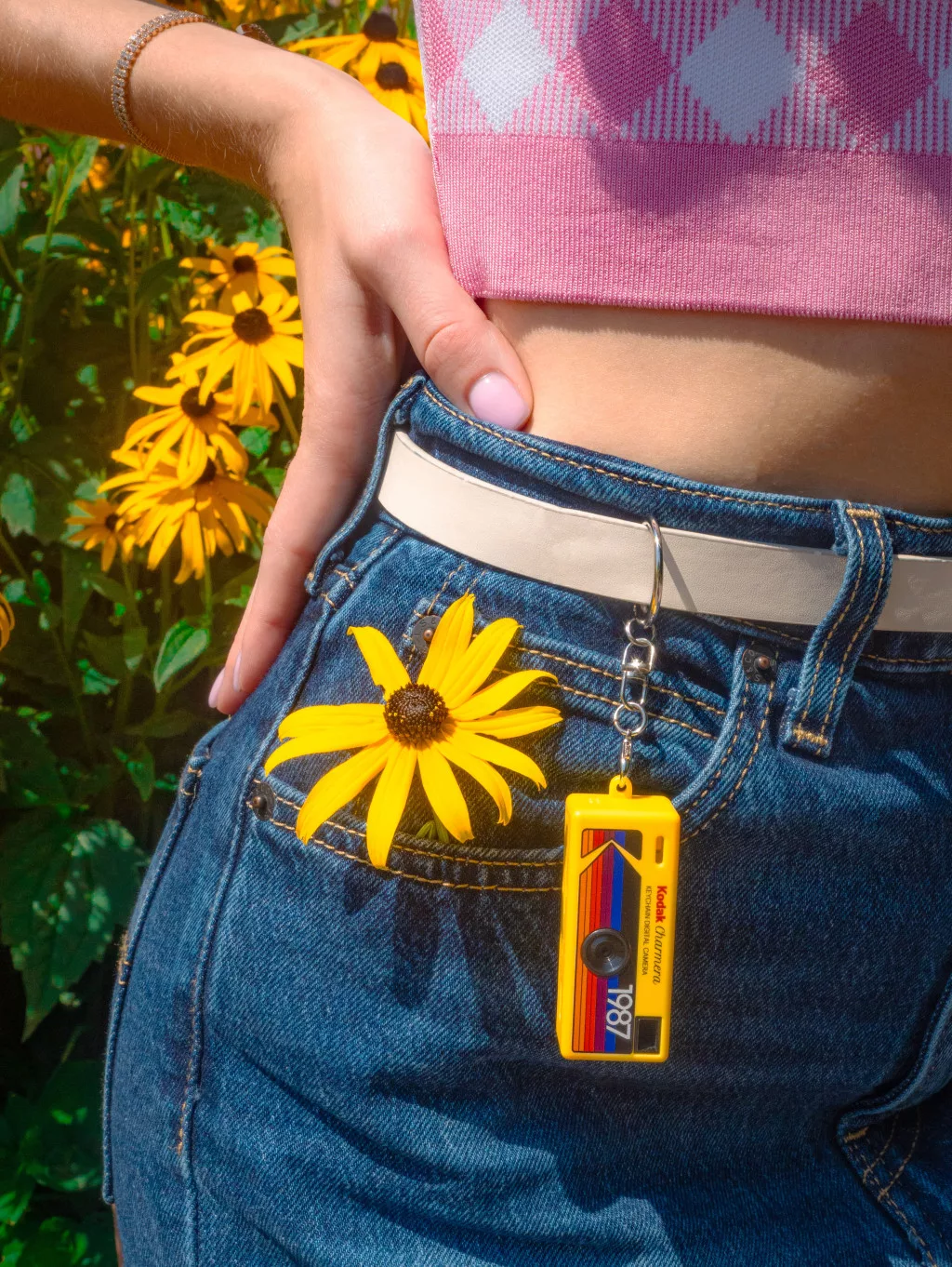 Farmerban és rózsaszín kockás felsőben lévő nő sárga Kodak Charm kulcstartót visel.