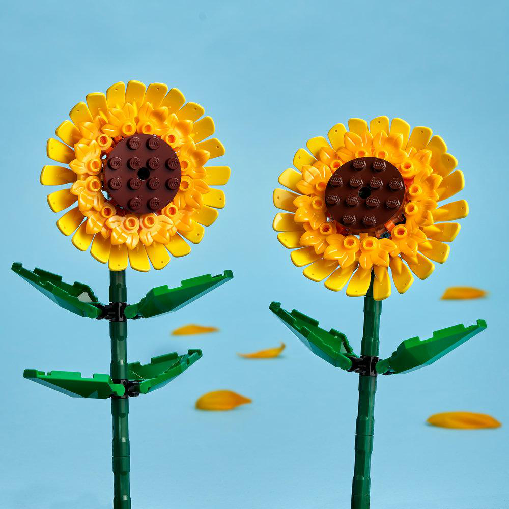 Zwei Lego-Sonnenblumen mit gelben Blütenblättern und grünen Blättern vor blauem Himmel.