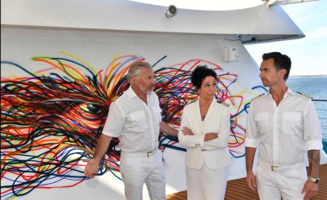 Drei Personen vor einer bunten Graffiti-Wand auf einem Schiff.