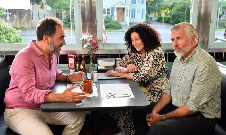 Drei Personen sitzen an einem Tisch in einem Diner. Draußen ist es hell.