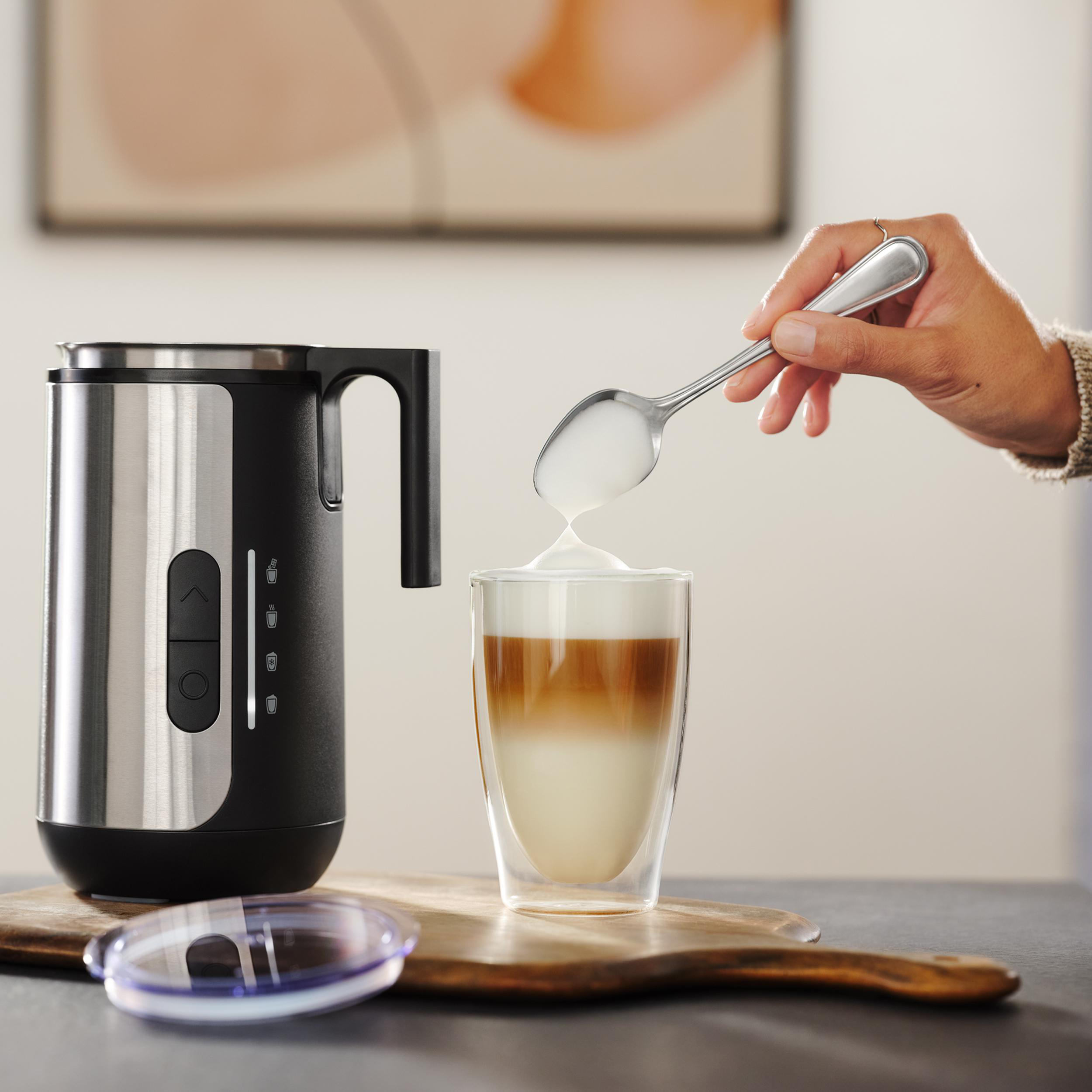 Milchaufschäumer neben Glas mit Kaffee und Milchschaum. Löffel mit Schaum.