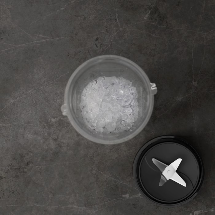 Szklanka z kruszonym lodem i czarna pokrywka z ostrzami na ciemnym kamieniu.