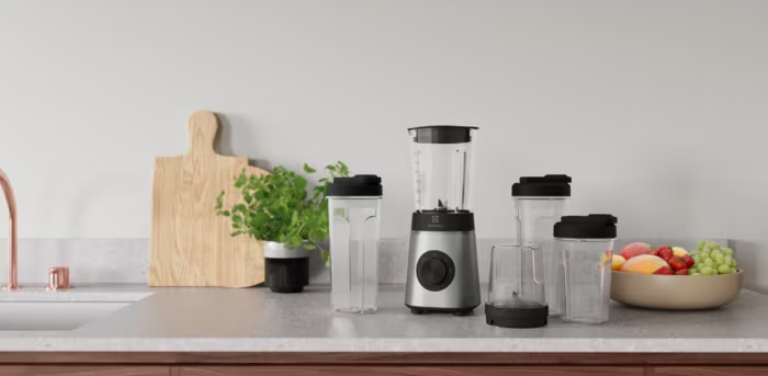 Srebrny blender z akcesoriami i miską owoców na blacie kuchennym.