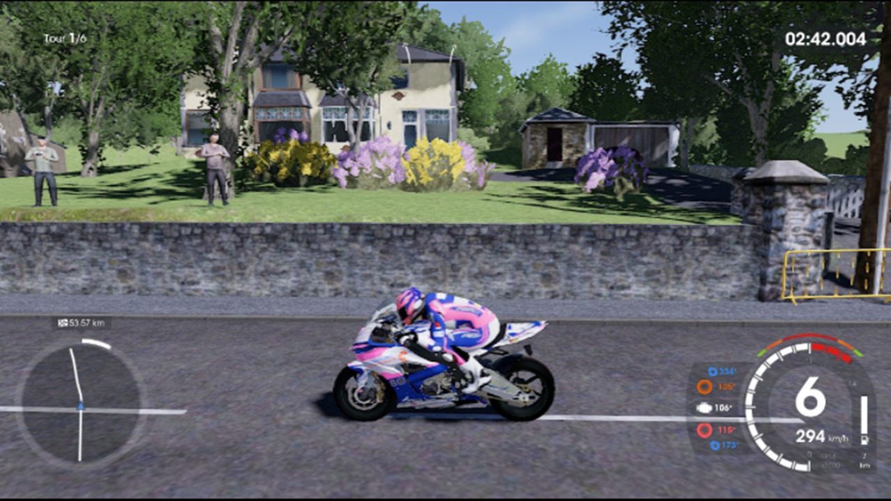 Motorradfahrer in Pink und Blau rast auf einer Straße an einem Haus vorbei.