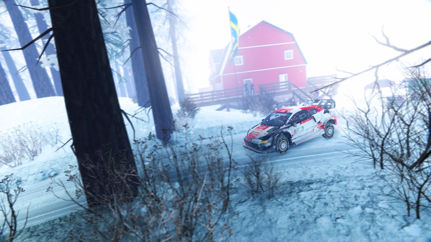 Ein rotes Rallyeauto fährt auf einer verschneiten Straße an einem roten Haus vorbei.