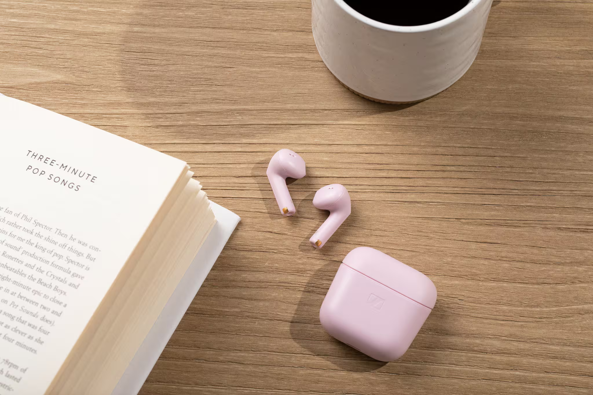 Un livre, des écouteurs roses et une tasse de café sur table bois.
