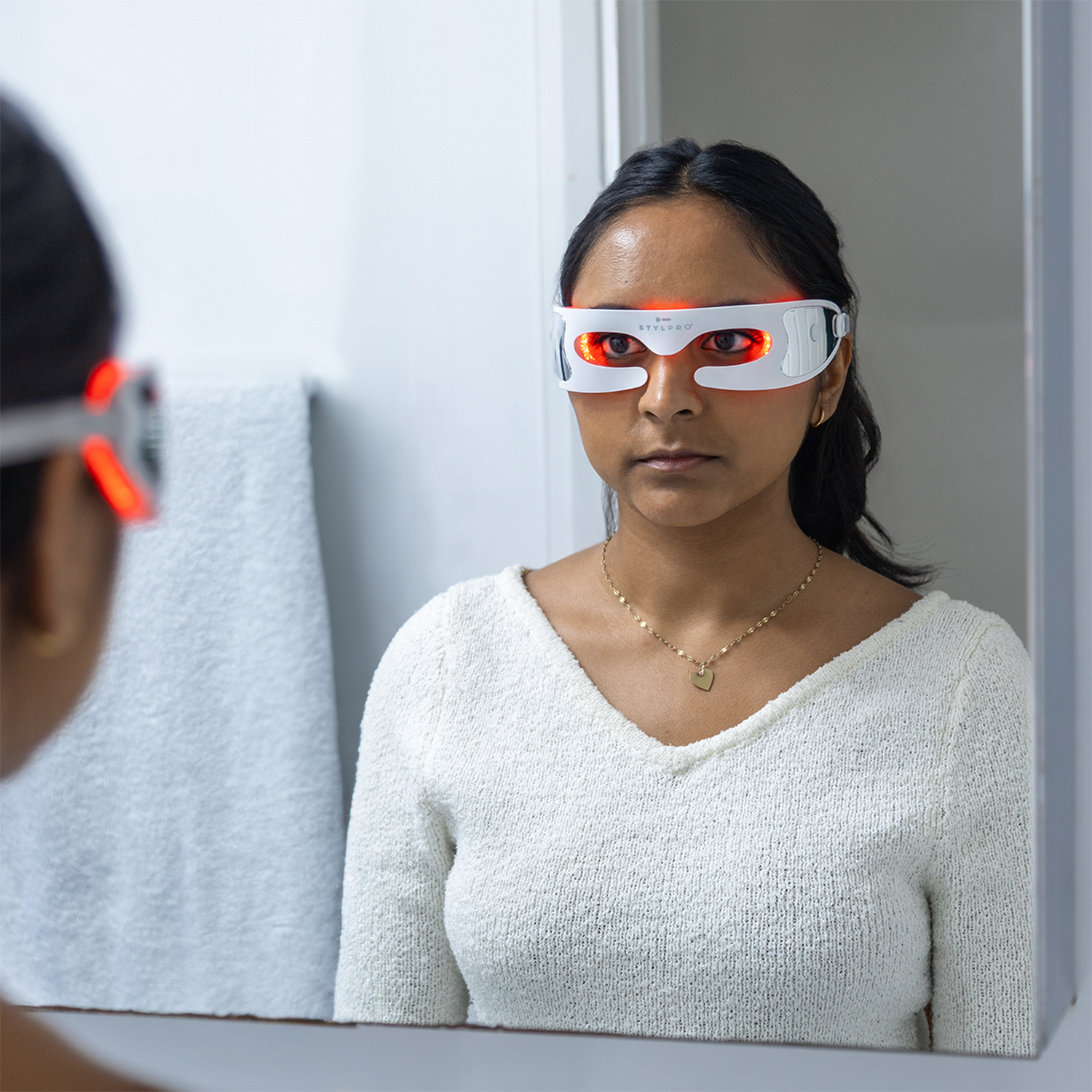 Mujer con máscara de ojos blanca y luces rojas, mirándose al espejo.