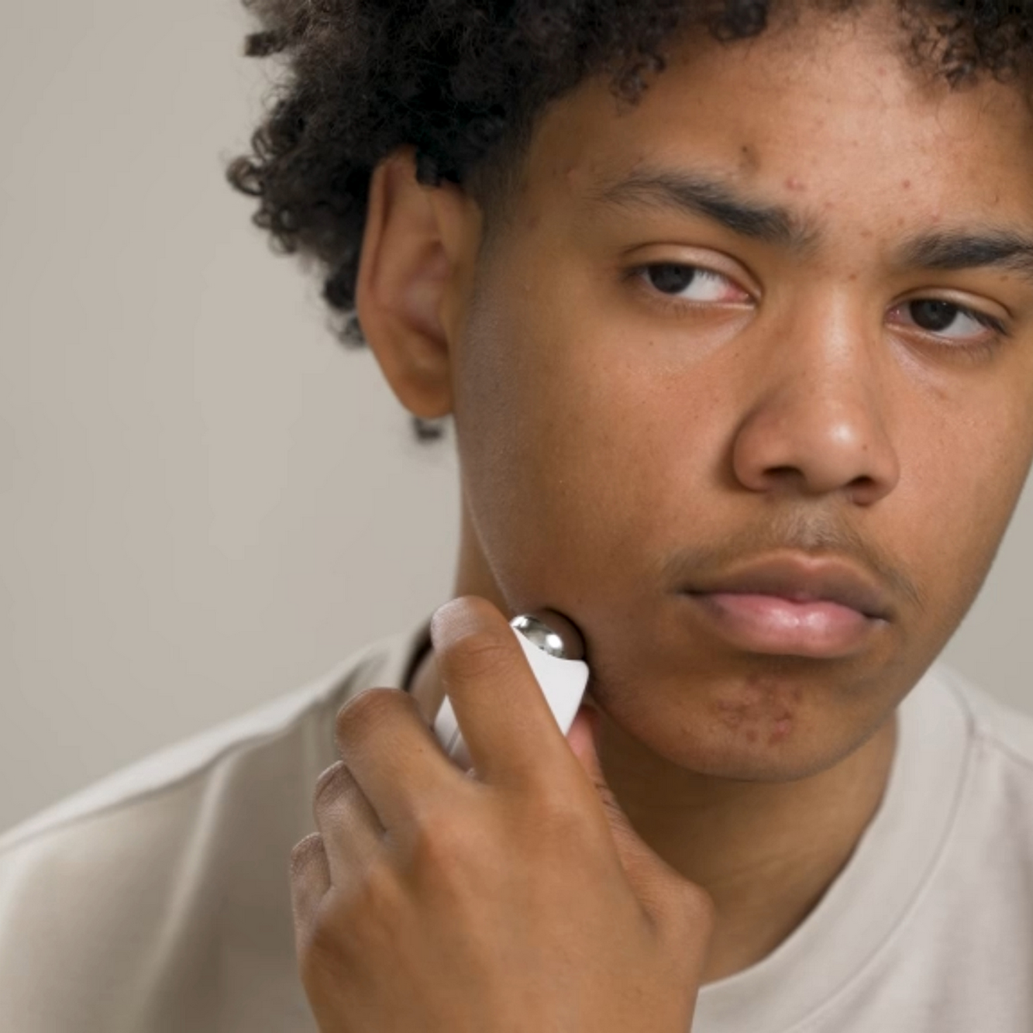 Un hombre joven con pelo rizado usa un pequeño dispositivo blanco en la cara.