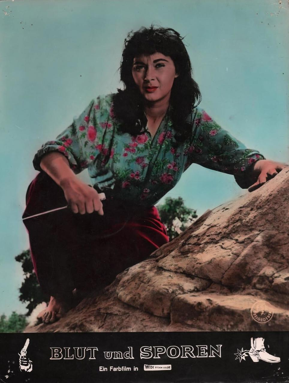 Frau in geblümtem Oberteil klettert auf Felsen.