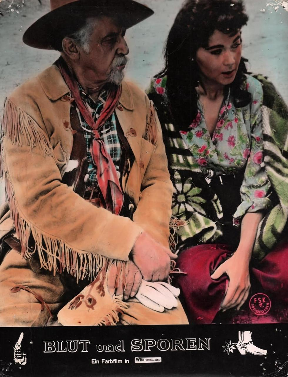 Ein Mann mit Hut und Fransenjacke und eine Frau mit Blumenhemd sitzen nebeneinander.