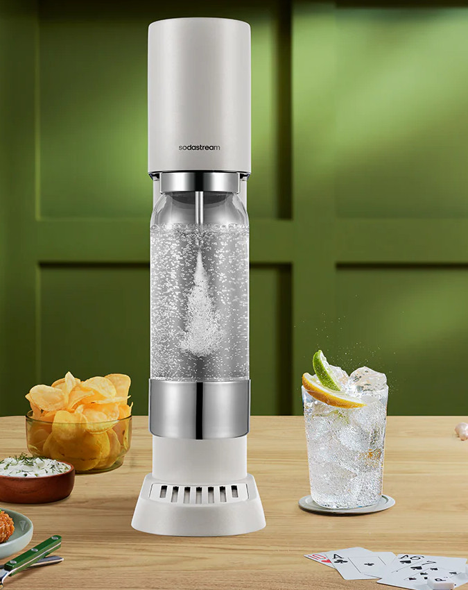 Urządzenie Sodastream na drewnianym stole z chipsami, dipem i napojem.