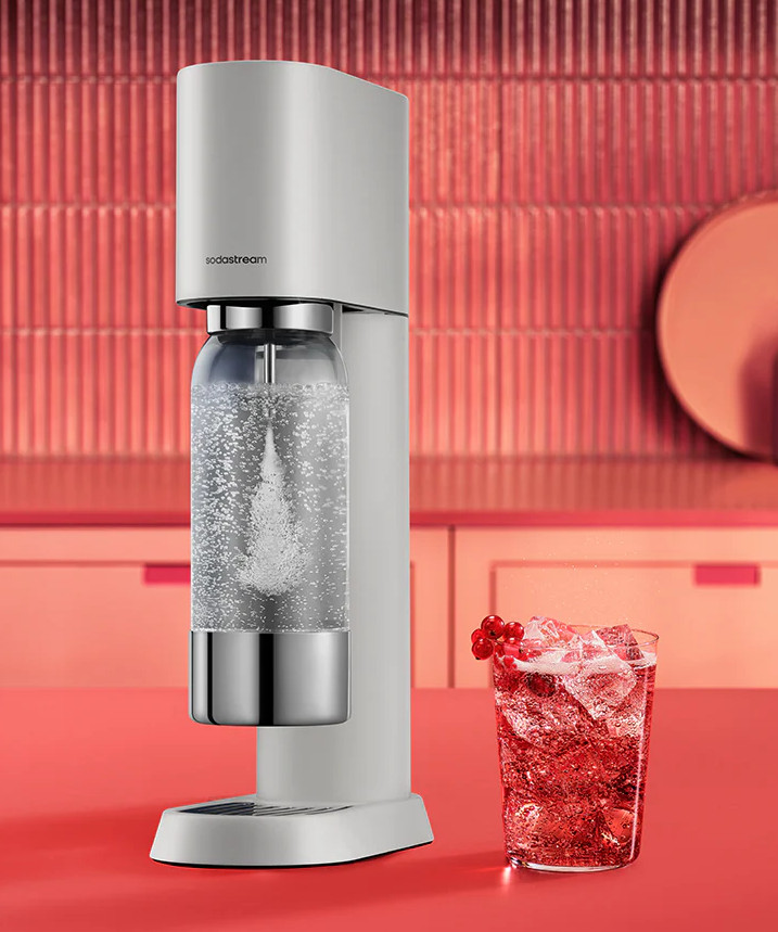 Urządzenie Sodastream nasyca wodę dwutlenkiem węgla w butelce obok szklanki czerwonego napoju.