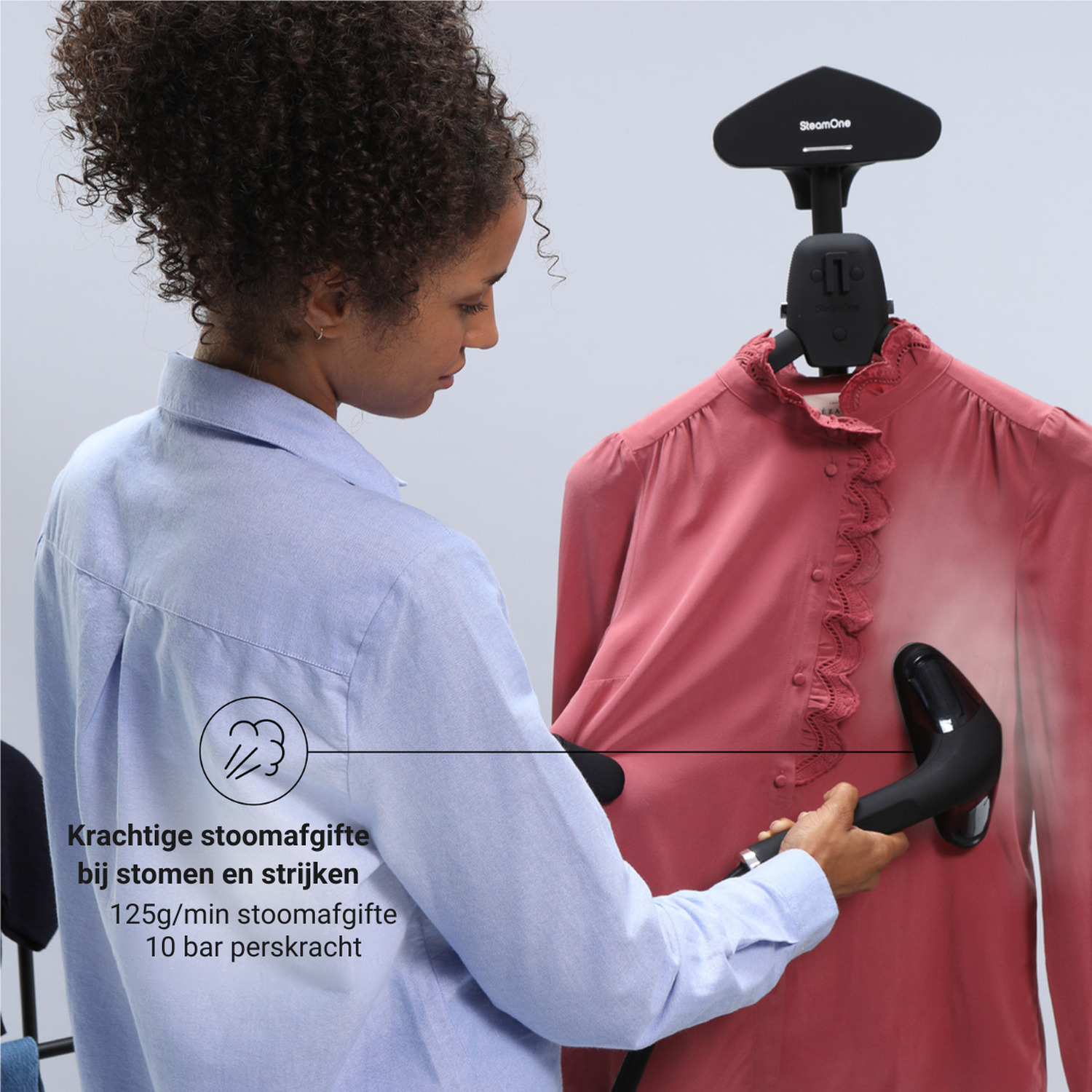 Een vrouw stoomt een roze blouse met een handstomer.