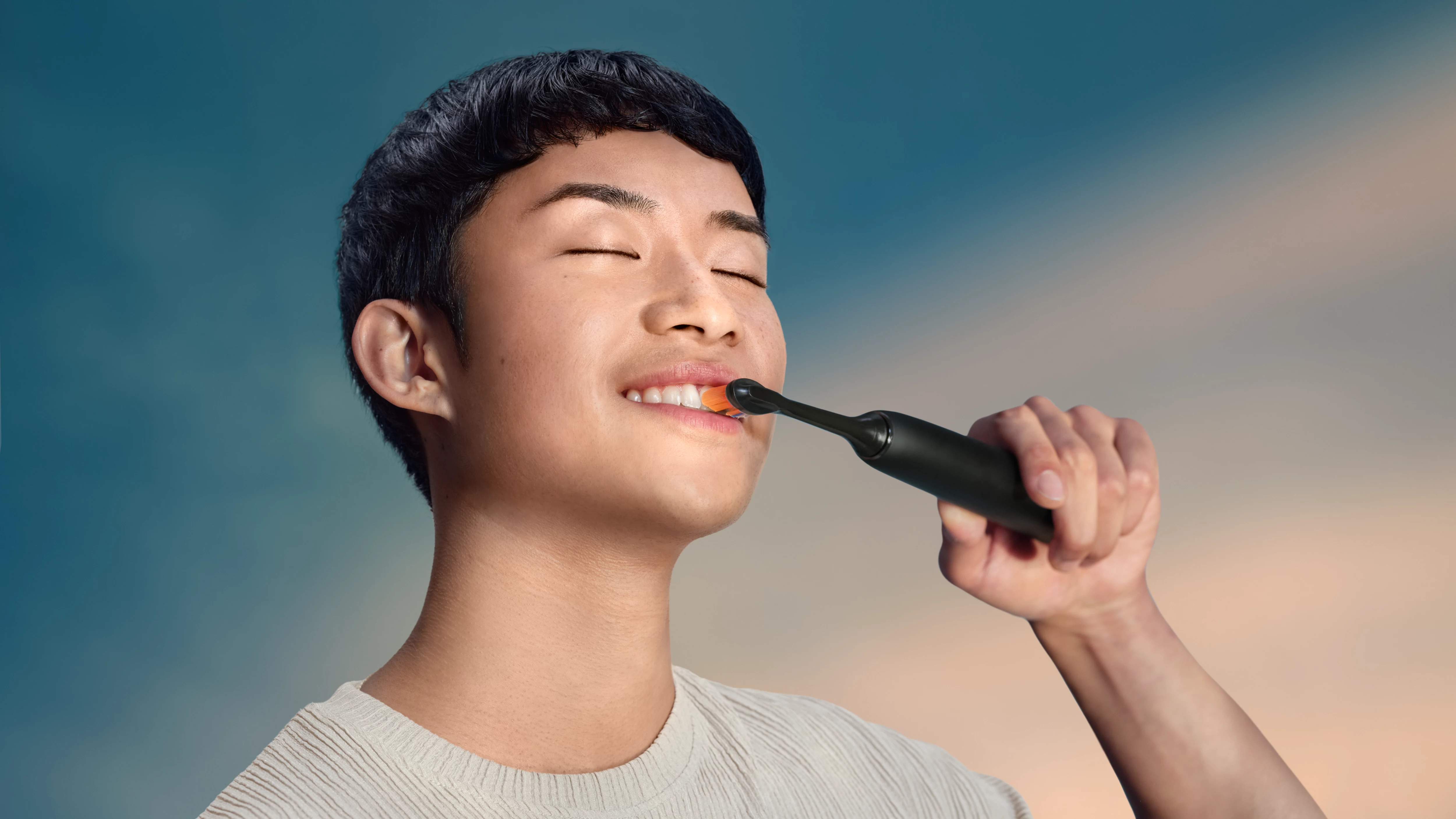 Młody mężczyzna myje zęby czarną szczoteczką elektryczną.