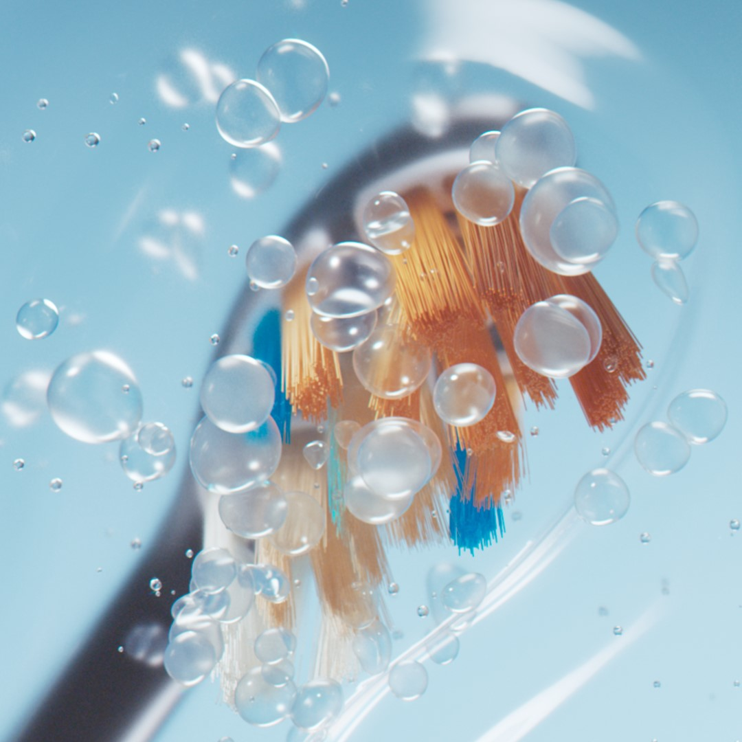 Zbliżenie szczoteczki elektrycznej z pomarańczowym włosiem i niebieskimi akcentami, otoczonej bąbelkami.