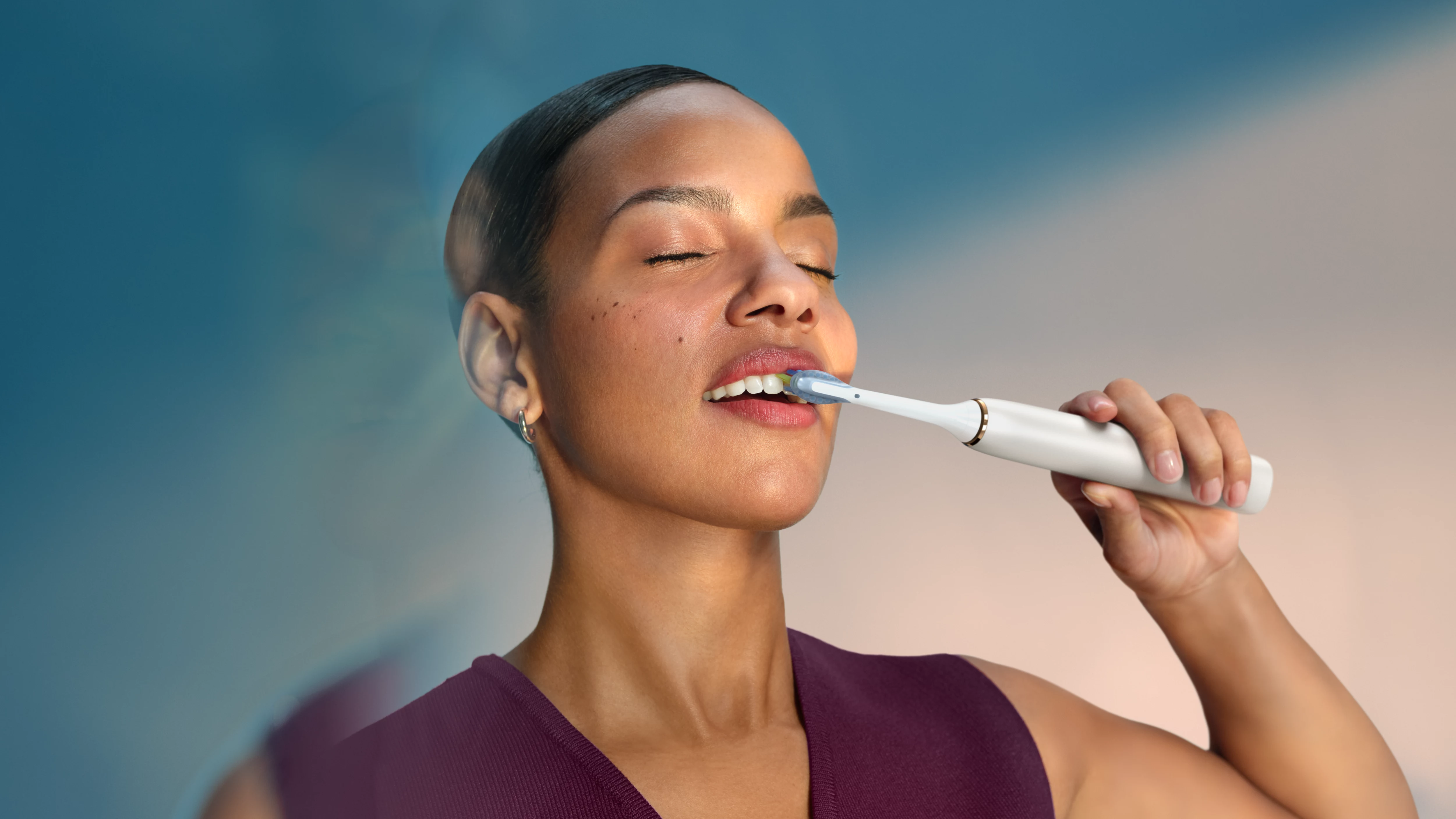 Kobieta myje zęby szczoteczką elektryczną na tle koloru niebieskiego.