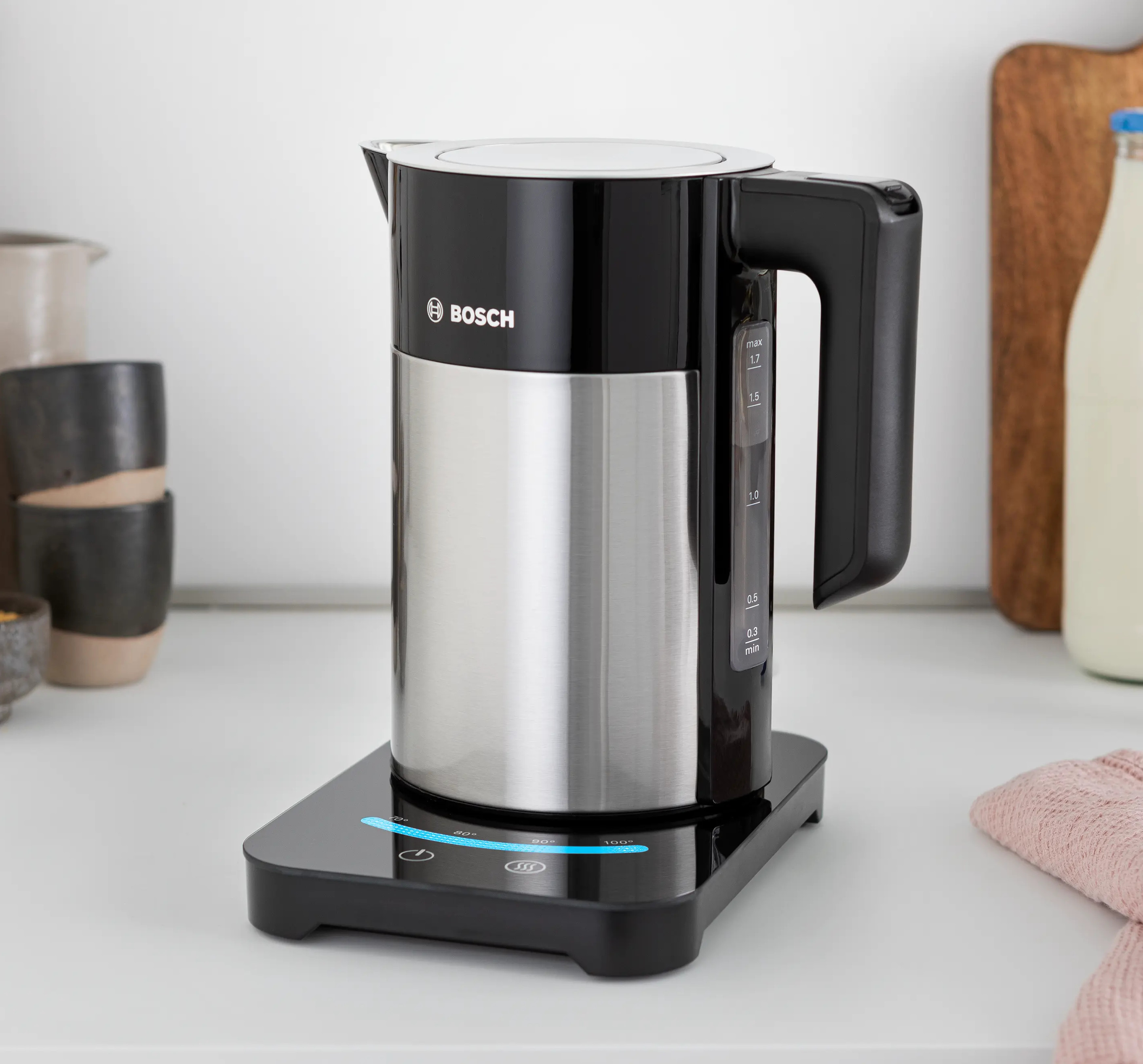Srebrny i czarny czajnik elektryczny Bosch stoi na czarnej podstawie z panelami dotykowymi.
