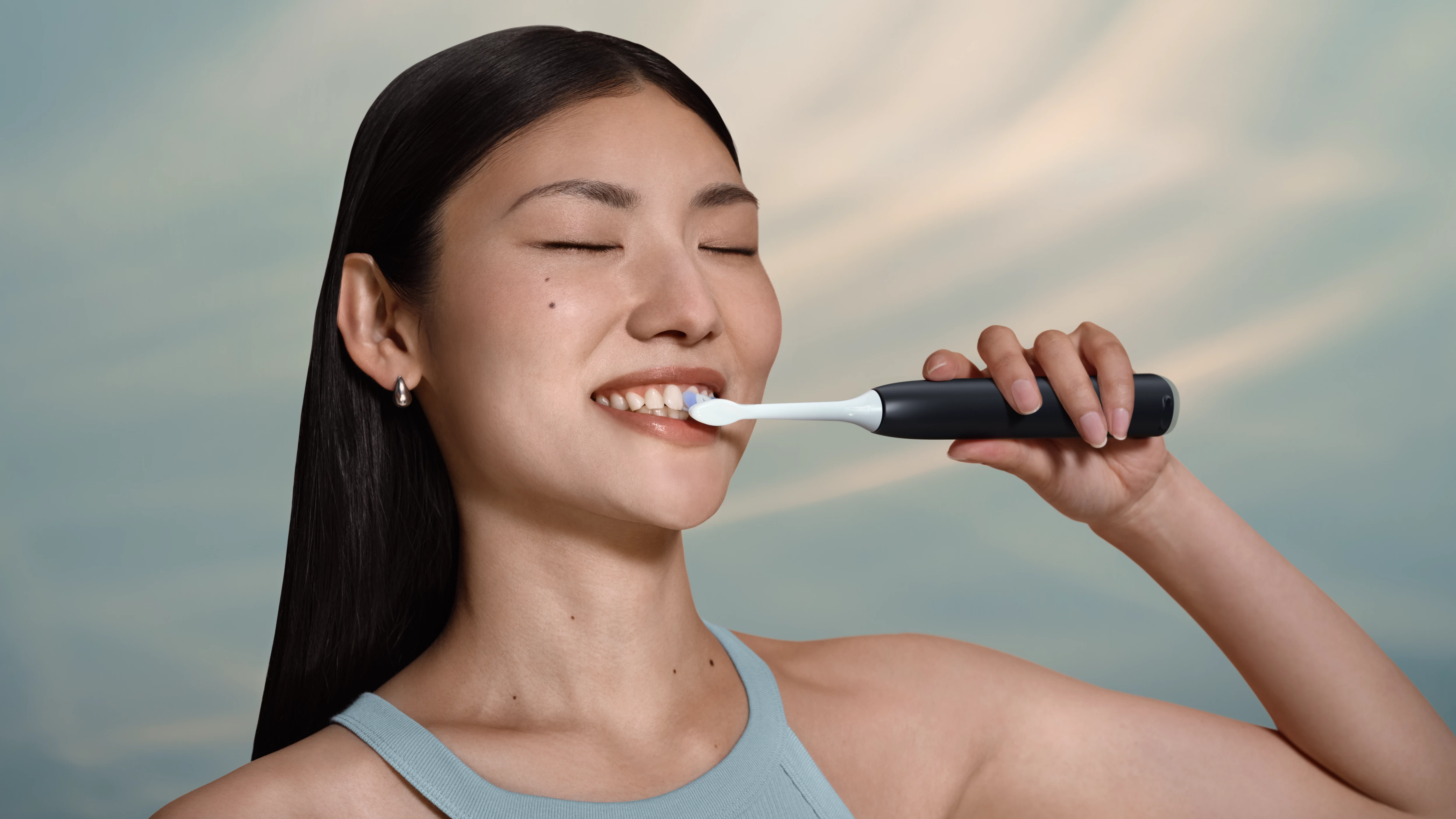 Kobieta myje zęby szczoteczką elektryczną.