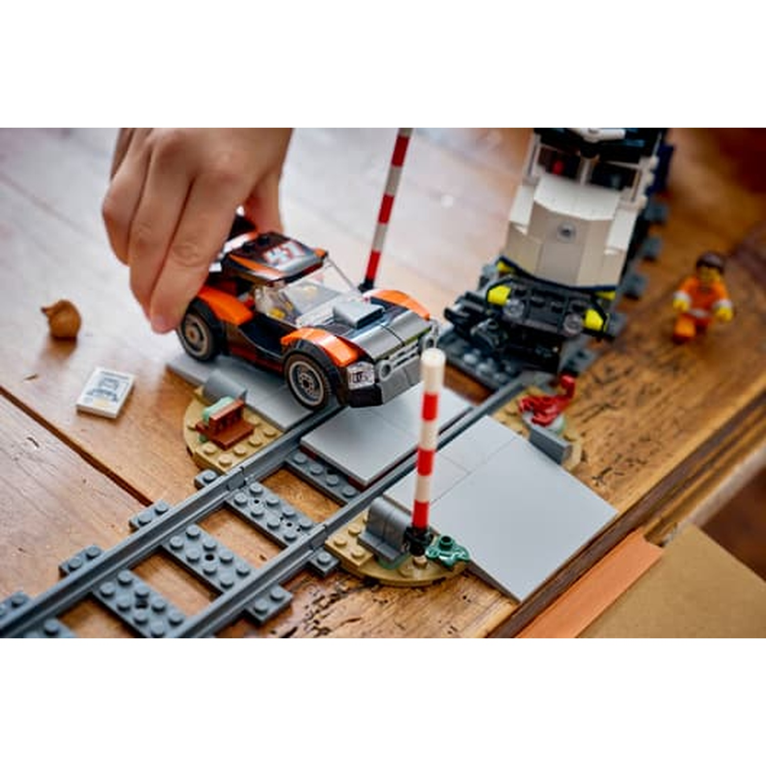 La mano di un bambino posiziona un'auto Lego arancione sui binari vicino a un treno e una figura Lego.