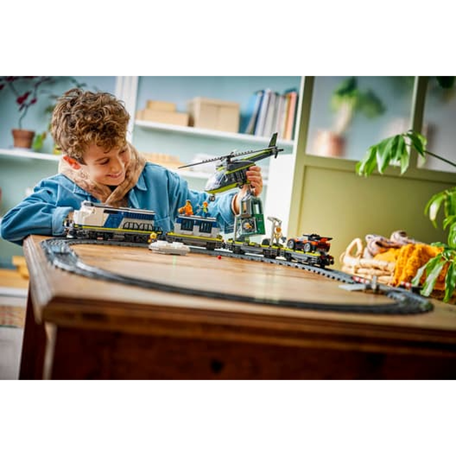 Un ragazzo gioca con un trenino Lego, tenendo un elicottero giocattolo. Include treno, binari, auto.