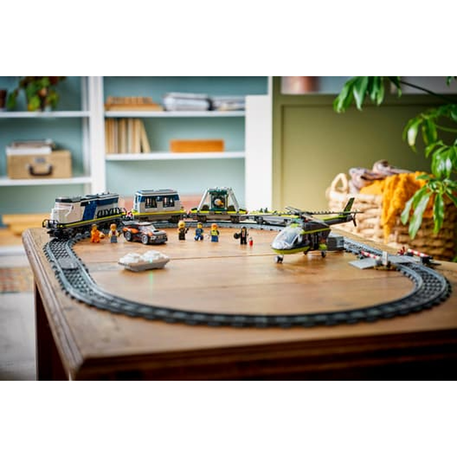 Treno Lego, elicottero, auto e figure su un binario per treni su tavolo di legno.
