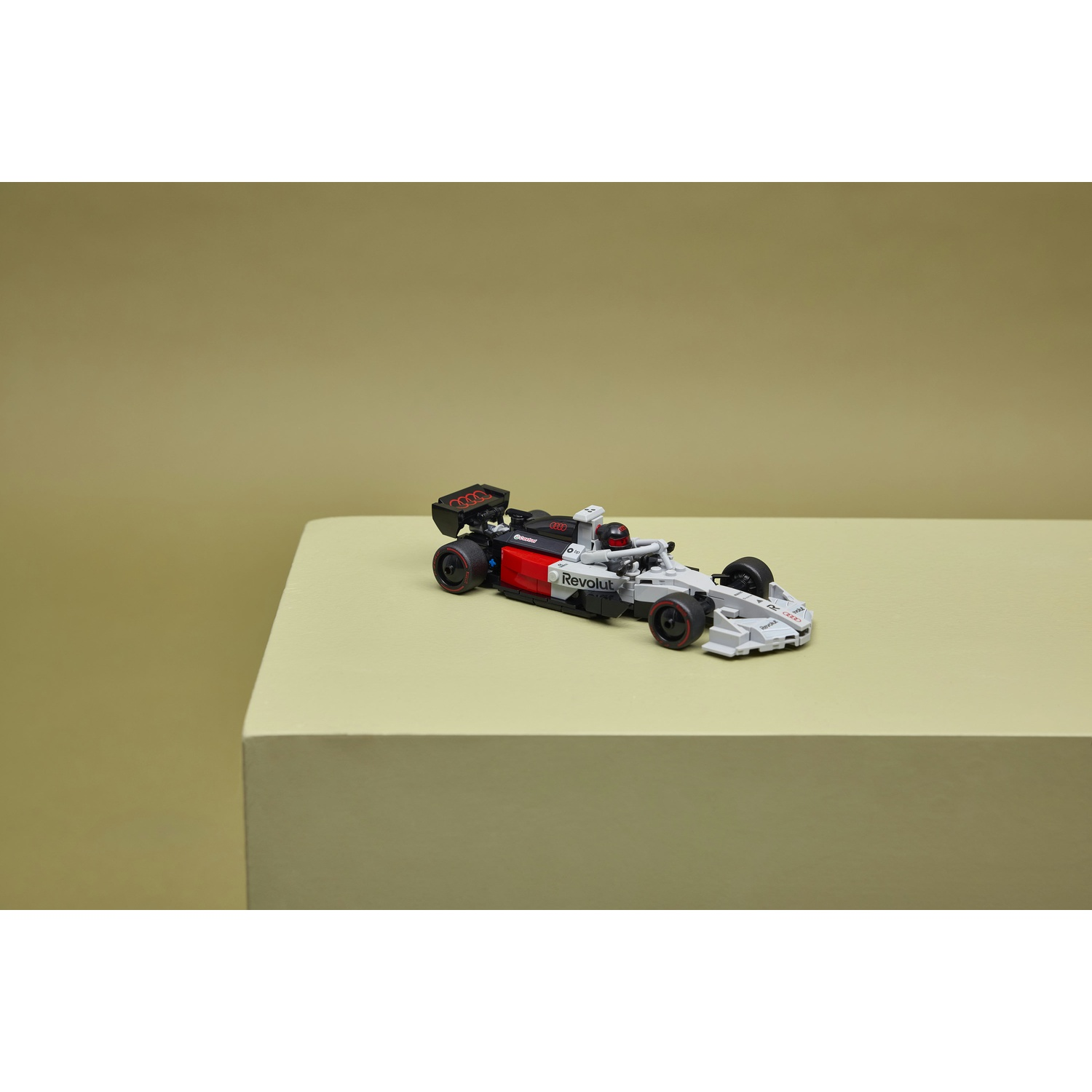 Un'auto Lego di Formula 1 grigia e rossa con ruote nere è su una superficie verde chiaro.
