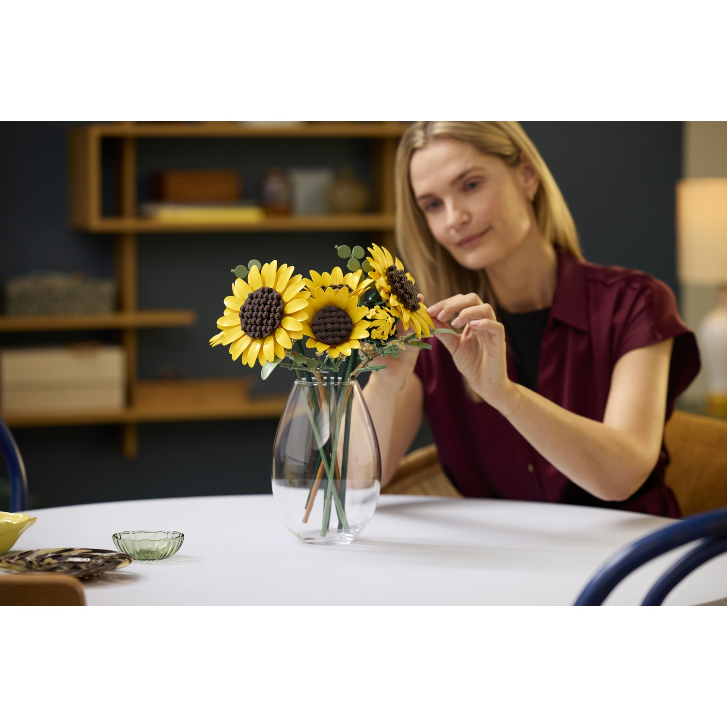 Donna sistema girasoli gialli in un vaso di vetro su un tavolo bianco.