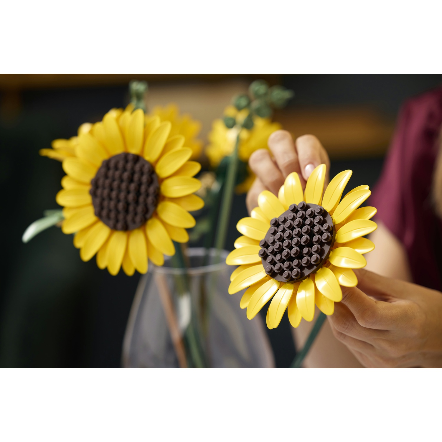 Mani tengono un girasole Lego giallo davanti a un bicchiere con altri girasoli.