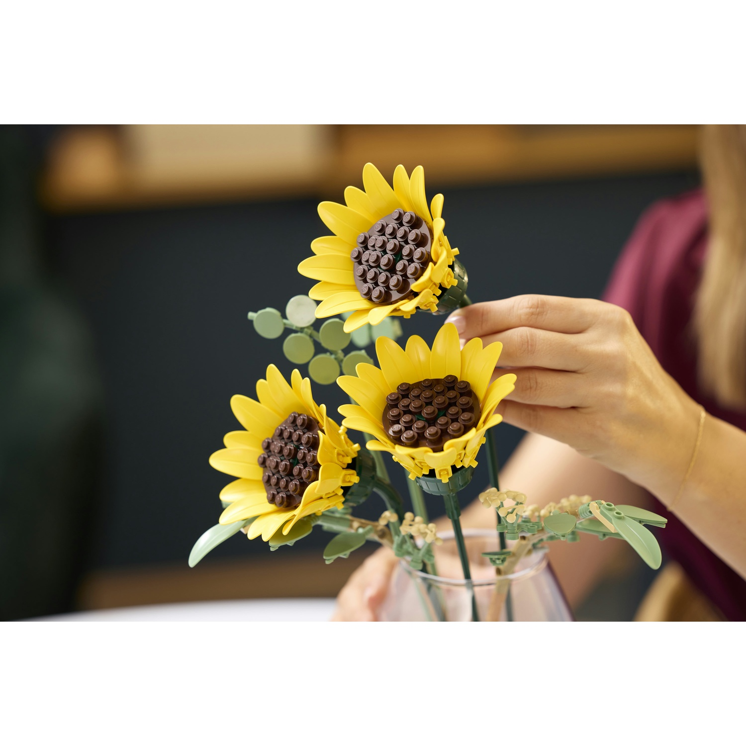 Girasoli gialli LEGO in un vaso di vetro, disposti da mani.