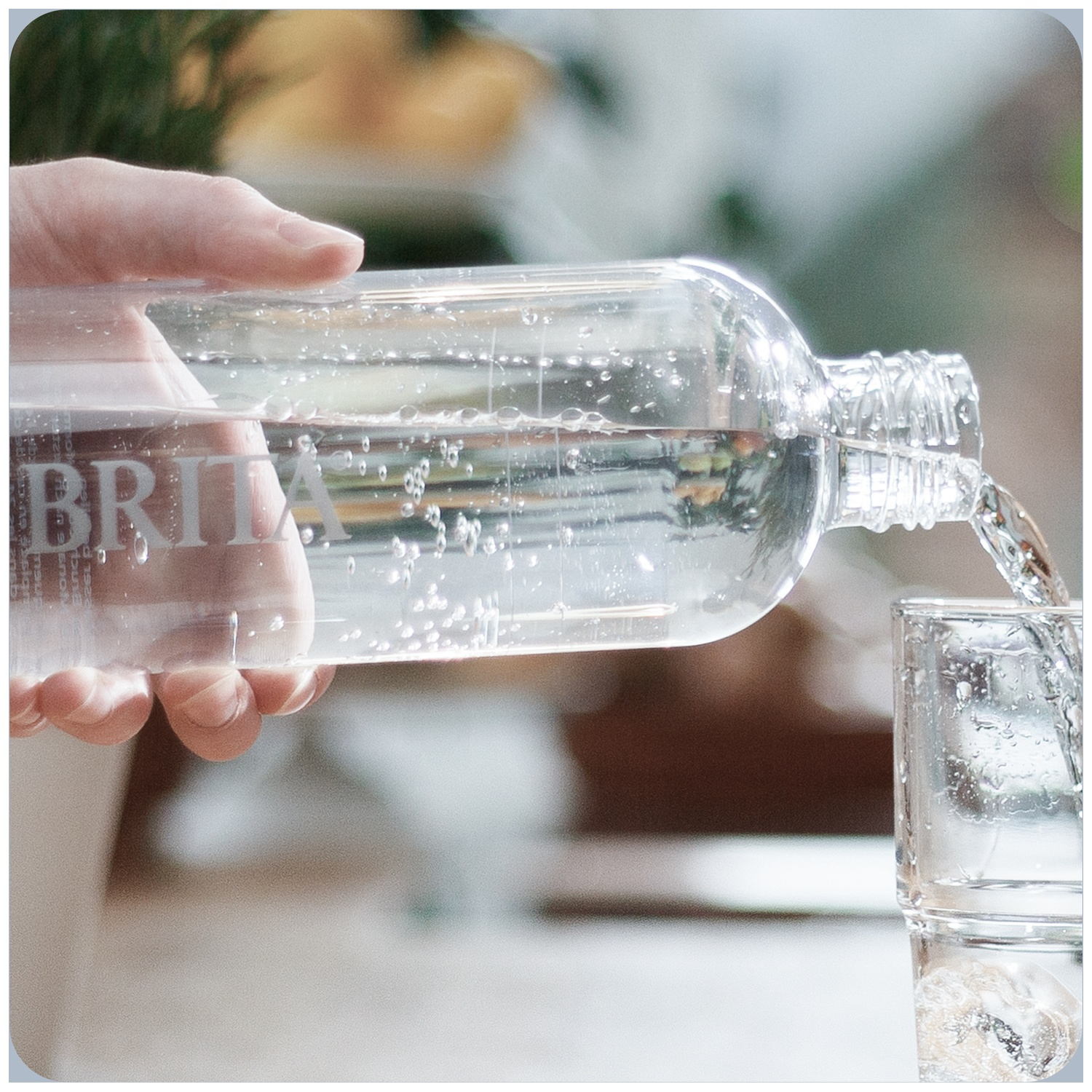 A hand pours clear water with bubbles from a Brita bottle into a glass with ice.