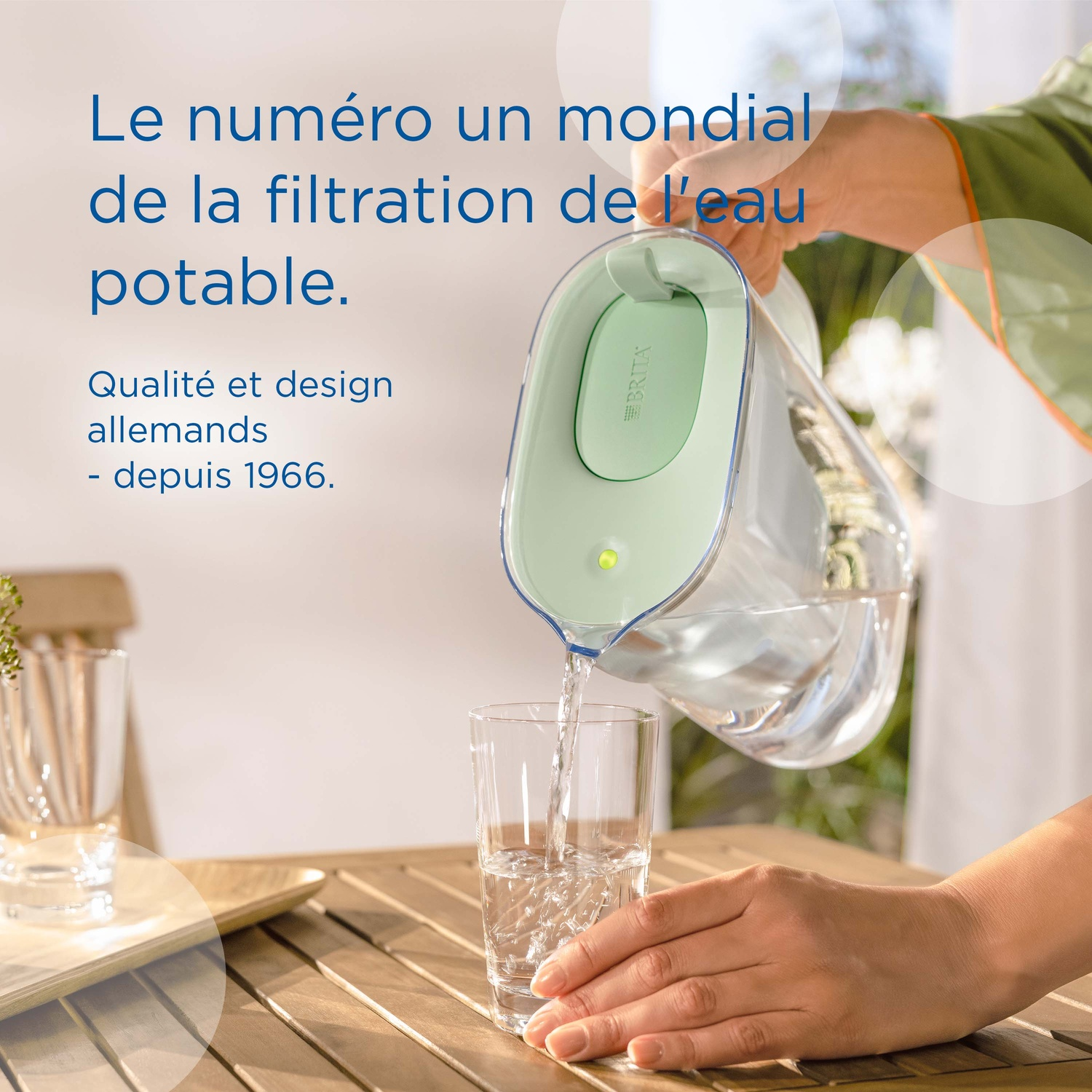 Een hand schenkt water uit een Brita-kan in een glas op een houten tafel.